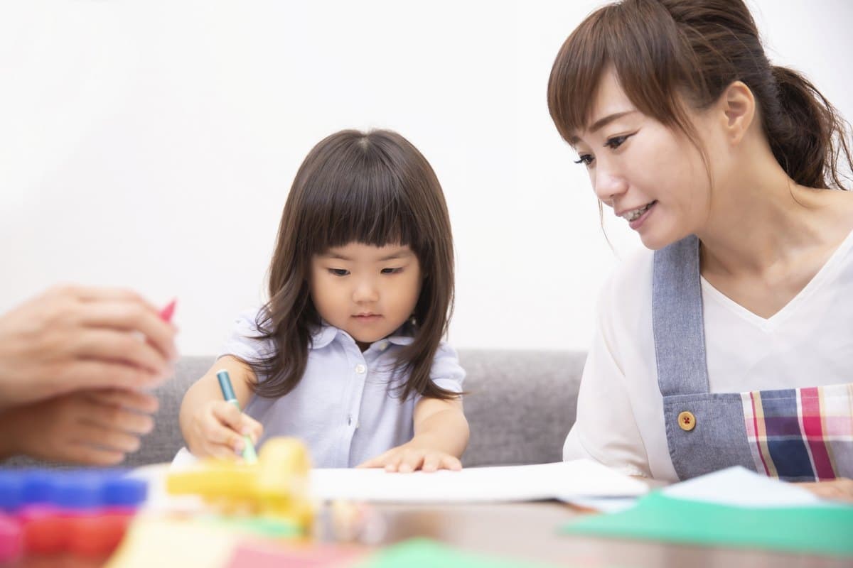 机に向かってお絵かきをする子どもを、笑顔で見守る職員